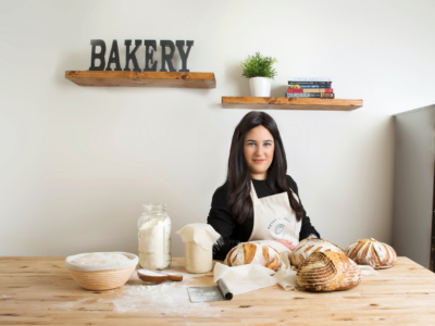 Woman with dark hair in apron smiling at baking table with sourdough bread ingredients