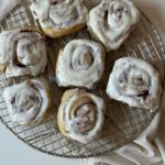 Fresh sourdough cinnamon buns on a cooling rack, topped with cream cheese frosting.