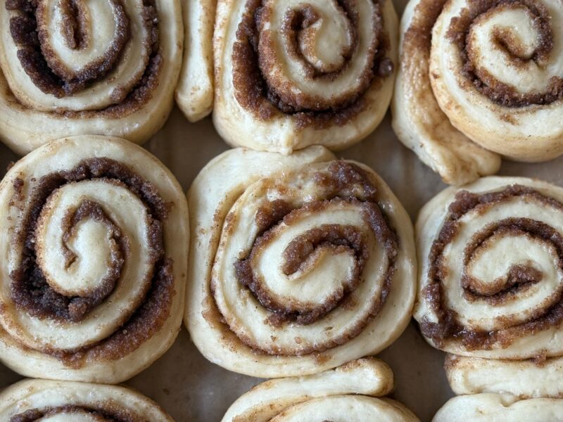 Unfrosted sourdough cinnamon rolls arranged in a pan, close‑up of cinnamon‑sugar swirls.