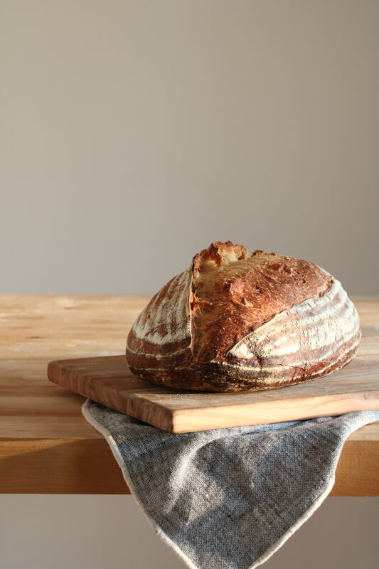A baked loaf of sourdough bread on a wood cutting board