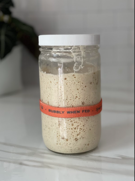 A jar of sourdough starter with a label that reads "bubbly when fed"