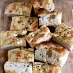 Fluffy sourdough focaccia slices on a cutting board, showing large air pockets and a crispy crust.