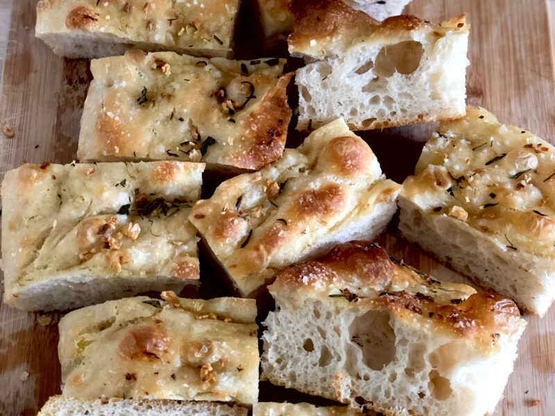 Fluffy sourdough focaccia slices on a cutting board, showing large air pockets and a crispy crust.