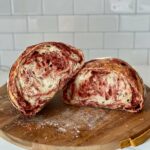 Sourdough bread with a vibrant red beet swirl, cut in half and displayed on a wooden cutting board.