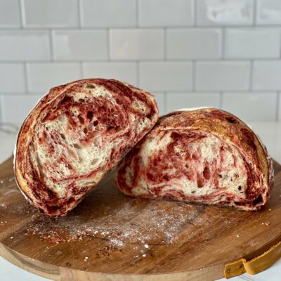 Sourdough bread with a vibrant red beet swirl, cut in half and displayed on a wooden cutting board.