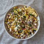 Overhead view of grilled corn and peach salsa in a white bowl with herbs and lime, bright and colorful summer side dish