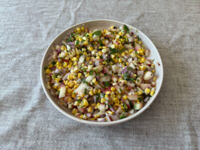 Grilled corn and peach salsa served in a bowl with fresh herbs and lime