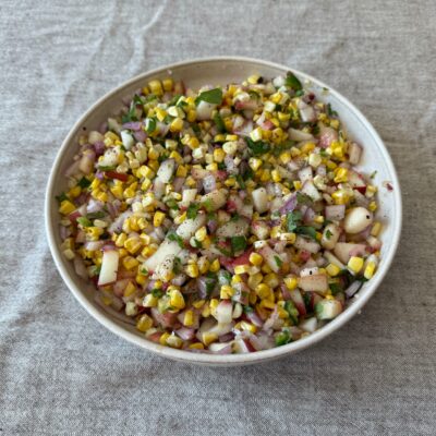 Grilled corn and peach salsa served in a bowl with fresh herbs and lime