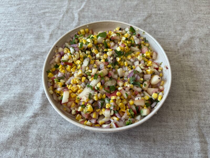 Grilled corn and peach salsa served in a bowl with fresh herbs and lime